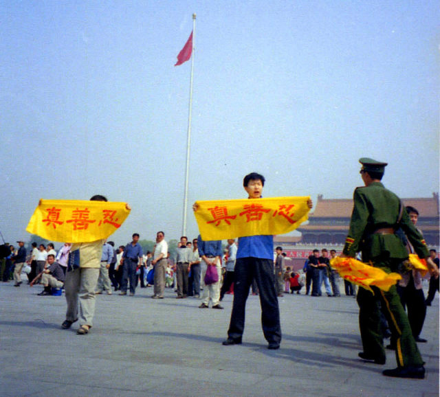 Falun Gong practitioners unfurl banners in Tiananmen Square in peaceful protest as a police officer approaches.